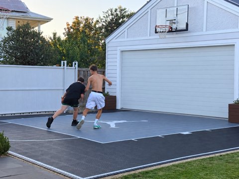 Two players in a one-on-one match on a backyard driveway basketball court