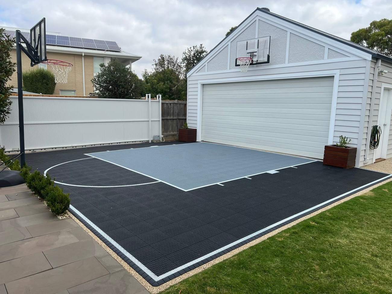 Charcoal and grey backyard half basketball court beside a garage
