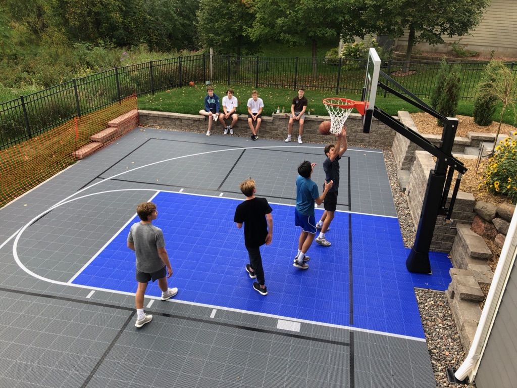 Backyard multi-sport court in blue and grey tiles with players shooting hoops