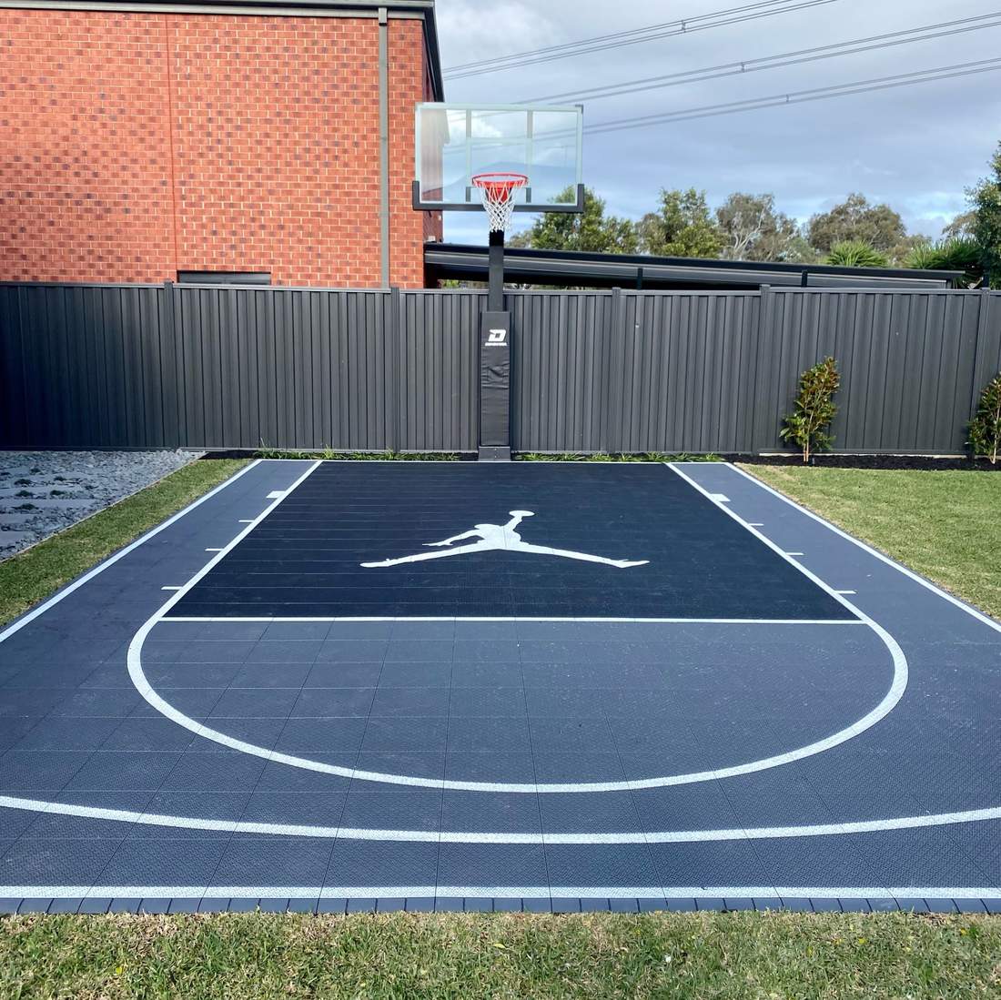 Dark custom size backyard basketball court with white lines and centre logo